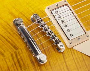 Close up of the aluminum stopbar and the bell-brass ABM tune-o-matic bridge of a Quarzo, amber flame top.